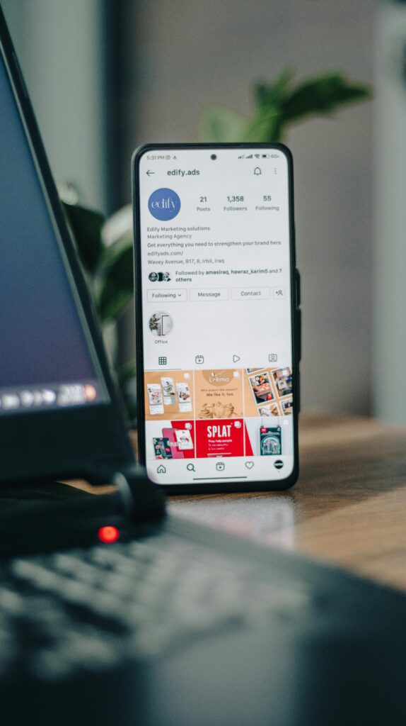 Vertical shot of a smartphone displaying an Instagram profile next to a laptop, representing social media engagement.